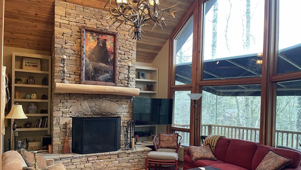 A cozy living room with a stone fireplace, a red sofa, a patterned rug, and a large window with a view of trees. - Casa Cortina: Eclectic Highlands Retreat w/ Covered Deck | 4 Min to Main Street (Highlands)