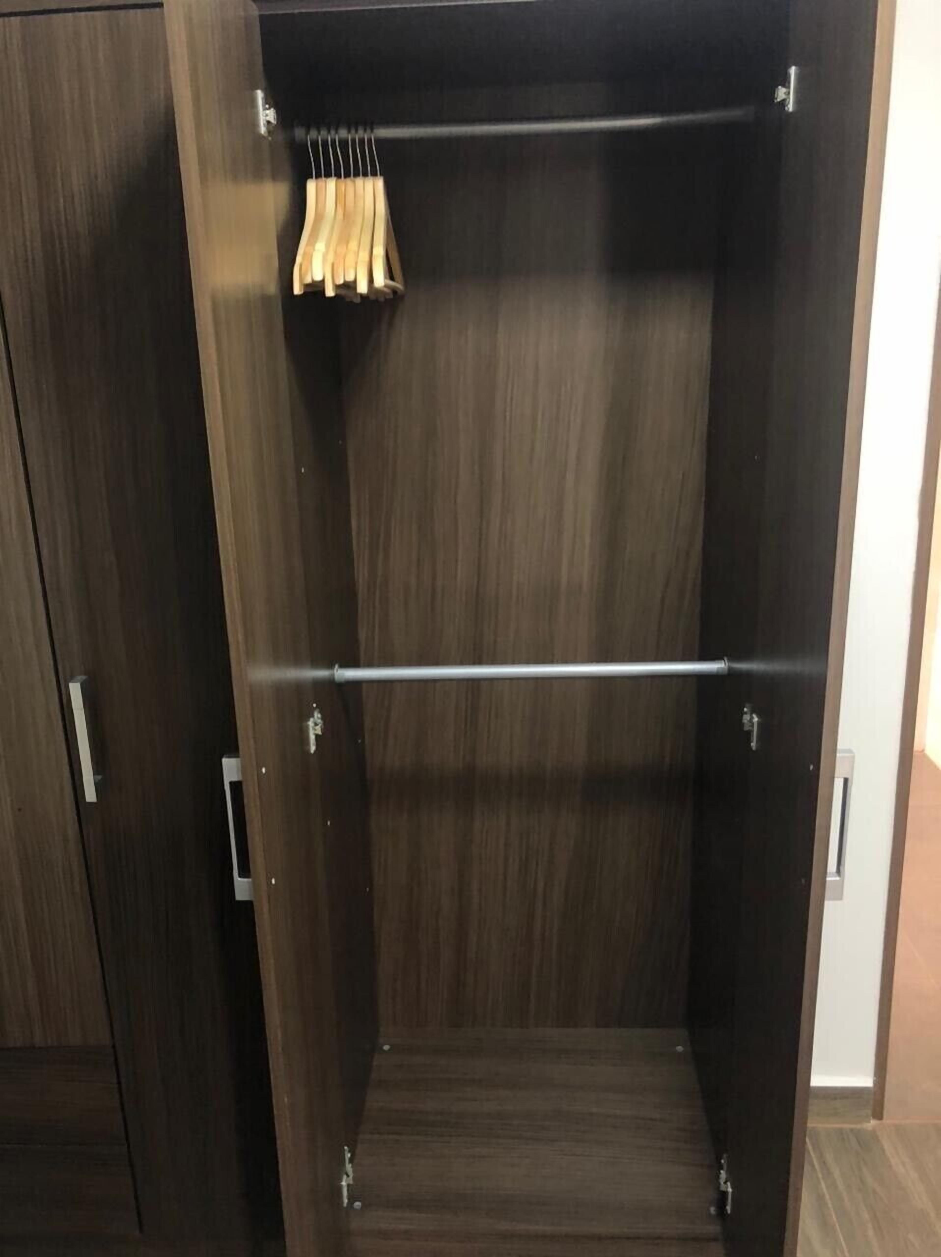 A dark wooden wardrobe with a metal rod and wooden hangers.