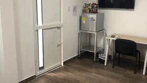 Una habitación con puerta corredera, un televisor de pantalla plana montado en la pared, un escritorio pequeño con una silla y un refrigerador.