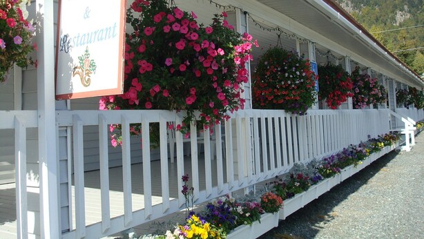 A building with a sign reading "Chilkat Bakery & Restaurant" and a white picket fence with hanging flower baskets.