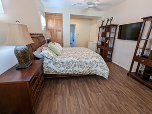 Ein Schlafzimmer mit einem Holzbett, einem Nachttisch mit Lampe, einer Holzkommode, einem Bücherregal und einem Fernseher.