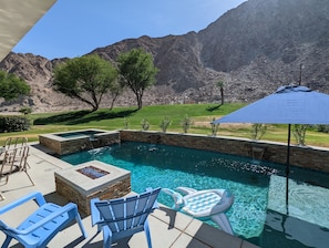 Una piscina con pareti in pietra, circondata da sedie e un ombrellone, con montagne sullo sfondo.