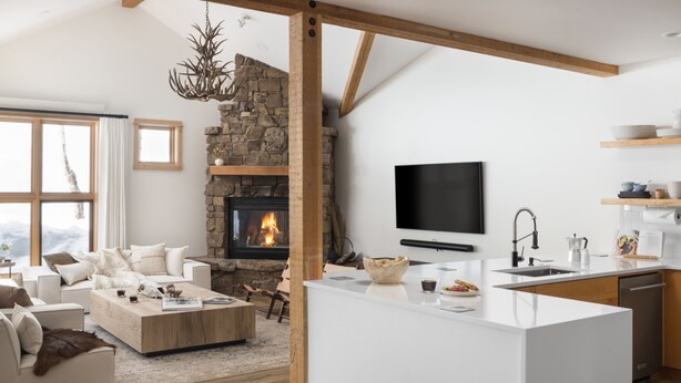 A modern living room with a stone fireplace, a flat-screen TV, and a kitchen island with a sink and counter. - Outpost: Moose Creek 25 - Private Hot Tub! (Teton Village)