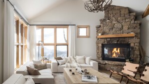 A cozy living room with a stone fireplace, large windows, and comfortable seating. - Outpost: Moose Creek 25 - Private Hot Tub! (Teton Village)