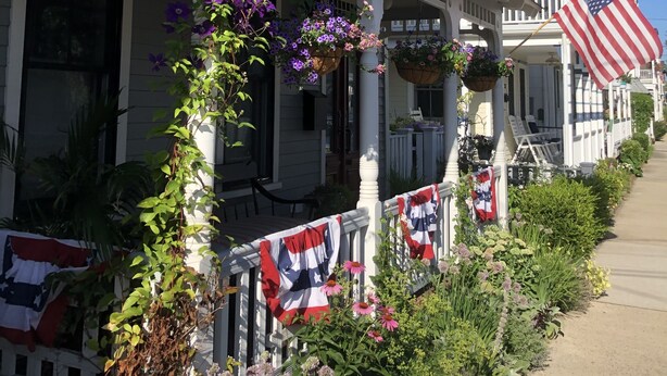 Een twee verdiepingen tellend huis met een veranda versierd met bloemen en Amerikaanse vlaggen.