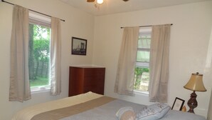 A bedroom with a bed, two windows with curtains, a wooden dresser, a lamp, and a framed picture on the wall. - 3blk St Mary 11to Mayo Pet Friendly CoveredByFaith (Rochester)