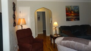 A living room with a red armchair, a grey sofa, and a painting of a sunset. - 3blk St Mary 11to Mayo Pet Friendly CoveredByFaith (Rochester)