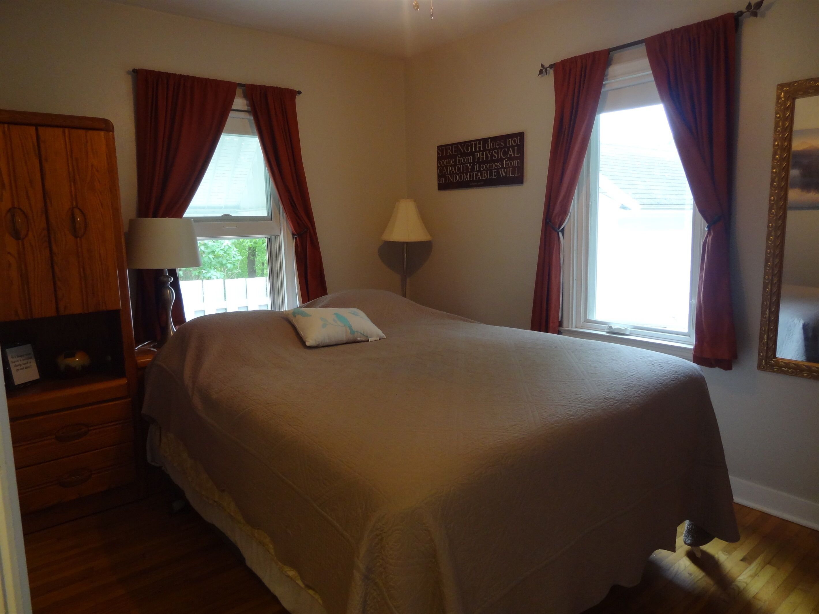 A neatly arranged bedroom with a large bed, two bedside tables, a lamp, and a motivational quote on the wall.