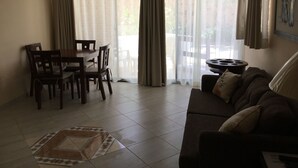 Ein Wohnzimmer mit Essbereich, einer Couch, einem Deckenventilator und Blick durch große, mit Vorhängen drapierten Fenster.
