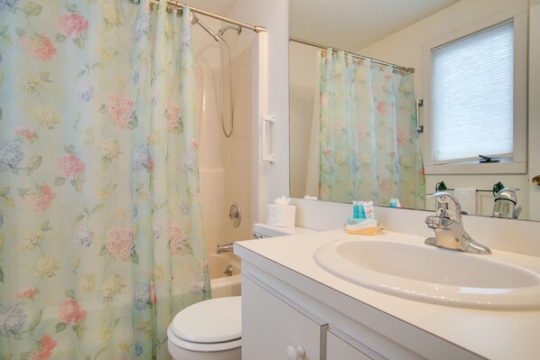 Une salle de bain avec un rideau de douche à motifs floraux, un lavabo blanc, un miroir et des toilettes.