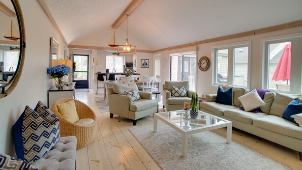 Een ruime woonkamer met een bank, fauteuils en een salontafel. Achtergrond is een zichtbare keuken.