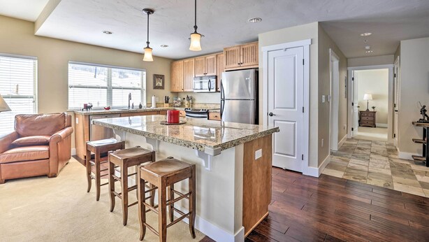 A spacious kitchen with a large island, wooden cabinets, and stainless steel appliances. There is a leather chair and bar stools near the island. - Ski-In/Ski-Out Granby Base Camp Escape w/ Balcony (Granby)