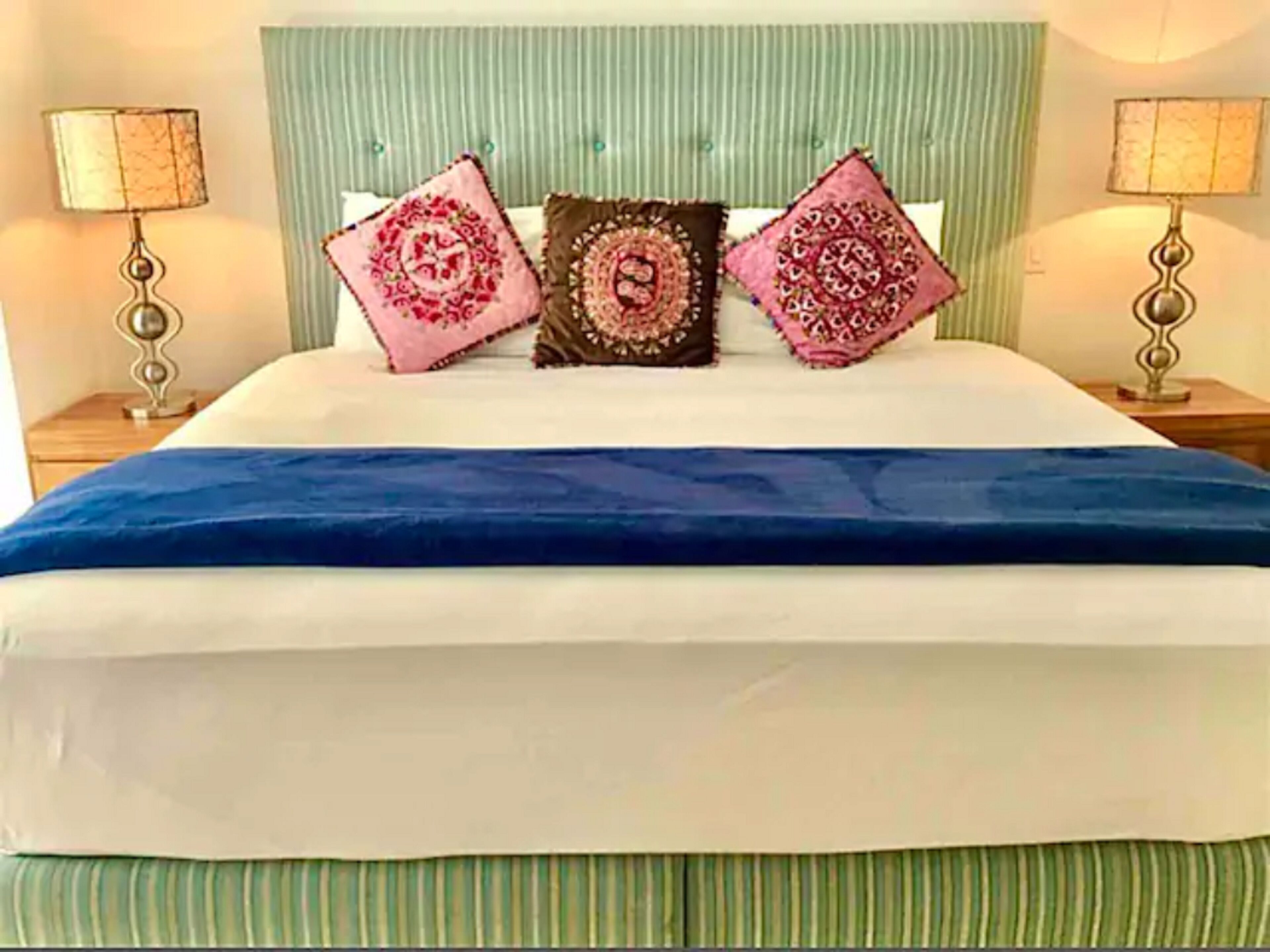 A bed with a blue bedspread, two nightstands with lamps, and three decorative pillows.