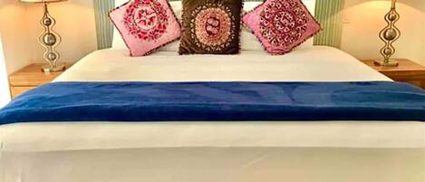 A bed with a blue bedspread, two nightstands with lamps, and three decorative pillows.