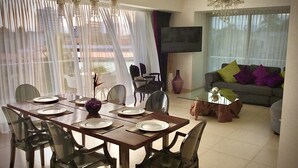 A dining area with a table set for four, chairs, a vase, and a TV in the background. - Icon Vallarta Apartments (Puerto Vallarta)