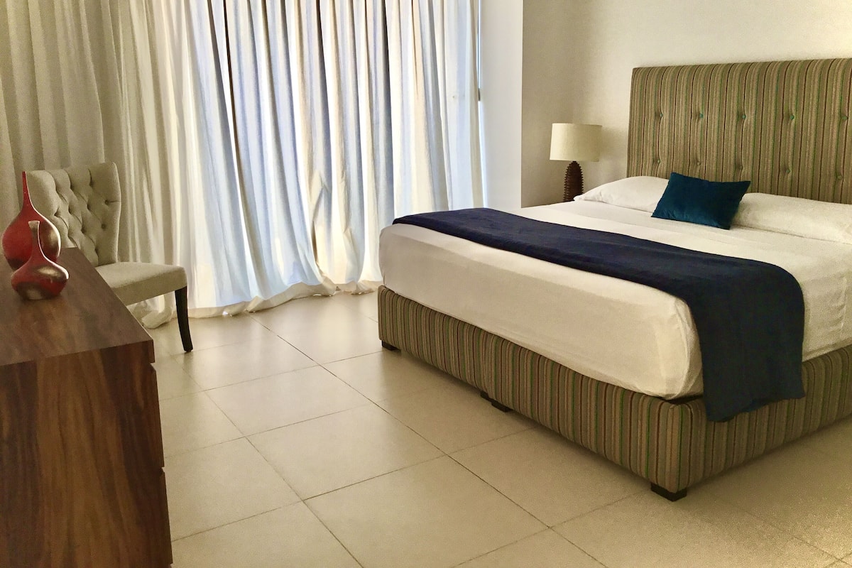 Une chambre d’hôtel avec un grand lit, une table de chevet, une chaise et une fenêtre avec des rideaux.