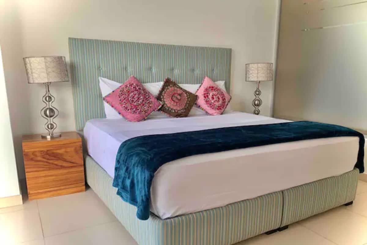 Un lit bien fait, avec une tête de lit à rayures, deux tables de chevet avec des lampes et un plaid bleu.