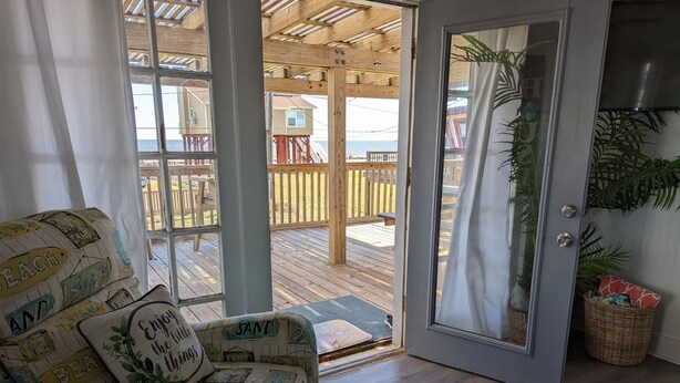 Ein Zimmer mit einer Holterrasse, einem gepolsterten Sofa mit Strandkissen und einer Tür zum Außenbereich.