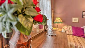 A wooden dining table with wine glasses and a bottle opener, a vase with red flowers, a lamp, and a floral cushion on a couch. - Pet-Friendly Apt: 2 Blocks to Riverside Park! (Yankton)
