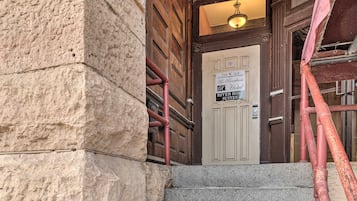 A hotel entrance with a stone facade, a wooden door, and a sign indicating '214 W 3rd The Riverfront Hotel River Rose Suites'.