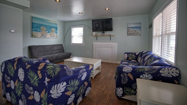 A living room with a grey sofa, a blue sofa with a tropical print, a white coffee table, and a TV mounted on the wall. - Fins Up Unit #1 - On The Bayside - Downtown - Spacious Unit! (Ocean City)