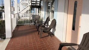 A covered porch with a tiled floor, white railing, and wooden chairs. - Fins Up Unit #1 - On The Bayside - Downtown - Spacious Unit! (Ocean City)