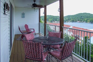 A covered outdoor area with a round table and four chairs, a ceiling fan, and a view of a lake and hills. - 'Serenity at the Lake' in Ozarks w/ View (Camdenton)