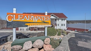 Skilt for 'Clearwater Condominiums' med udsigt til et hus og et vandareal i baggrunden.