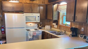 Une cuisine avec des meubles de rangement en bois, un plan de travail blanc, un réfrigérateur, un four à micro-ondes, une cuisinière, un grille-pain et une machine à café.