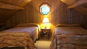 Une chambre mansardée chaleureuse, avec deux lits, une petite table et une fenêtre.