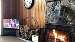 Un salon chaleureux avec une cheminée en pierre, un téléviseur et une pile de bois de chauffage.