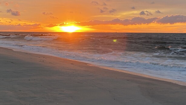 Ein Strand mit Wellen und einem Sonnenuntergang.