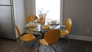 A dining area with a glass table, four yellow chairs, and a vase with flowers.