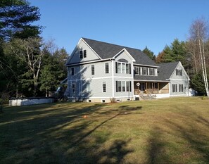 Stunning two-story house with a central entrance and two wings, set amidst a serene and lawn surrounded by mature trees.
