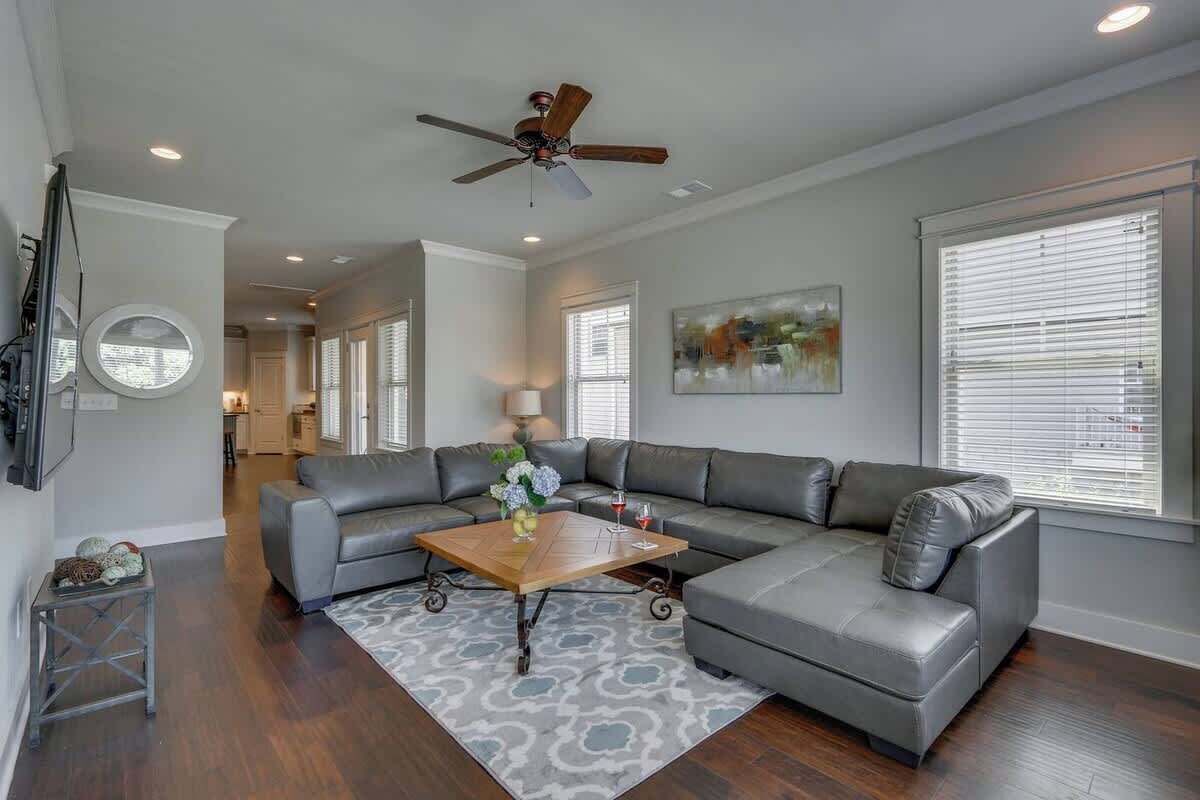 A spacious living room with a gray sectional sofa, a wooden coffee table, and a ceiling fan.
