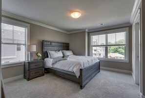 Cozy bedroom with a dark wood bed, nightstand, and lamp, featuring a window with blinds and a carpeted floor.