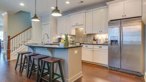 Una cocina moderna con armarios blancos, un refrigerador de acero inoxidable y una barra con taburetes.
