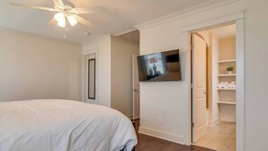 Un dormitorio con cama, ventilador de techo, televisión montada en la pared y armario con estantes.