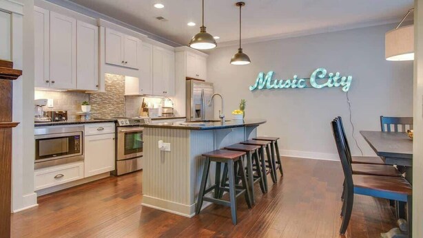 Una cocina moderna con armarios blancos, una isla central con taburetes y un letrero de neón que dice "Music City".