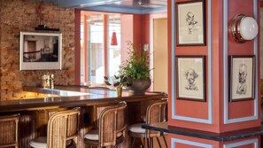 A bar area with wicker chairs, a bar counter, and framed artwork on the walls.