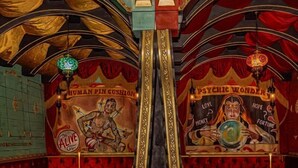 A bar with a mural of a muscular figure holding swords, a sign reading 'PSYCHIC WONDER,' and a green neon sign.