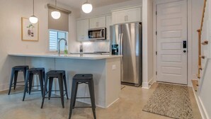 A modern kitchen with a central island, bar stools, stainless steel appliances, and pendant lighting.