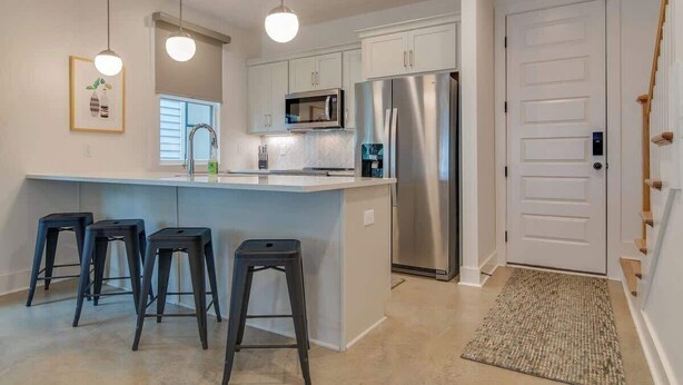 A modern kitchen with a central island, bar stools, stainless steel appliances, and pendant lighting. - East Nashville, Flexible Group Layout, 2 CarGarage |  2 Car Garage, Smart TVs in Every Room,  Near Five Points, The Gulch And 10 min to Broadway, 24 Hr Hospitality (Nashville)