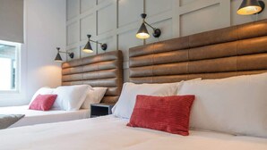 A hotel room with two beds, each with a headboard and bedside lamps.