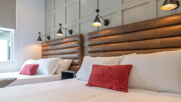 Ein Hotelzimmer mit zwei Betten, jeweils mit Kopfteil und Nachttischlampen.