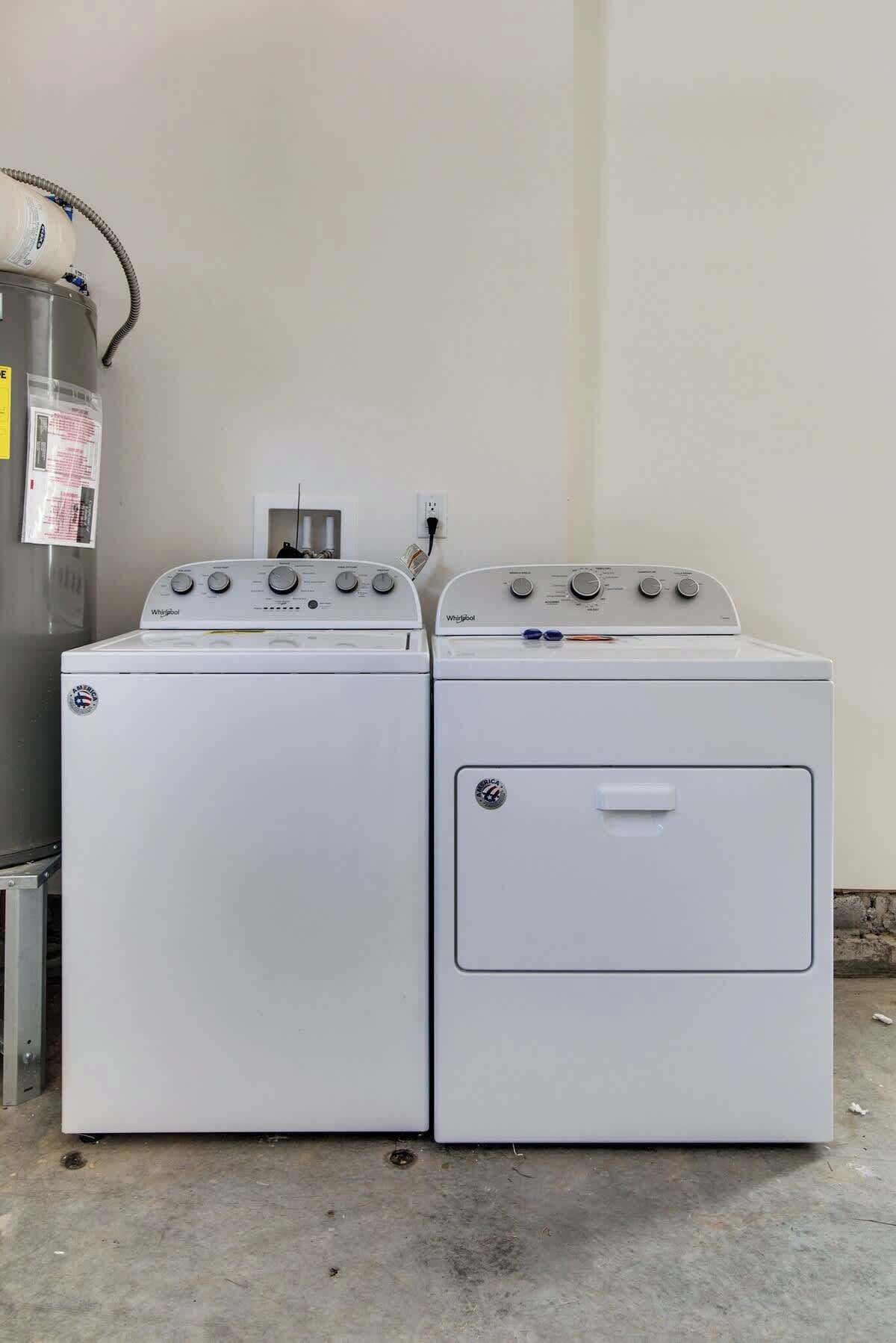 Two stacked front-loading Whirlpool washers in a utility room with a concrete floor and a white wall.