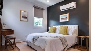 Een slaapkamer met een bed, een bureau en een stoel. Er zijn twee ramen en een airconditioning op de muur.