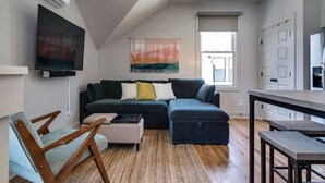Een moderne woonkamer met een hoekbank, een houten stoel, een bijzettafeltje en een tv aan de muur.