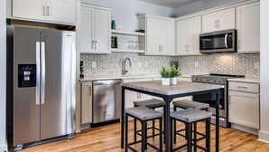 Een moderne keuken met witte kastjes, roestvrijstalen apparatuur, een centraal eiland met krukken en een backsplash van hexagonale tegels.