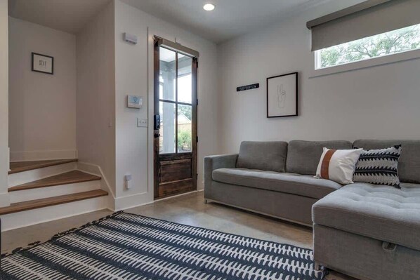 Una sala de estar moderna con un sofá gris, un tapete estampado y una escalera que lleva a otra habitación.
